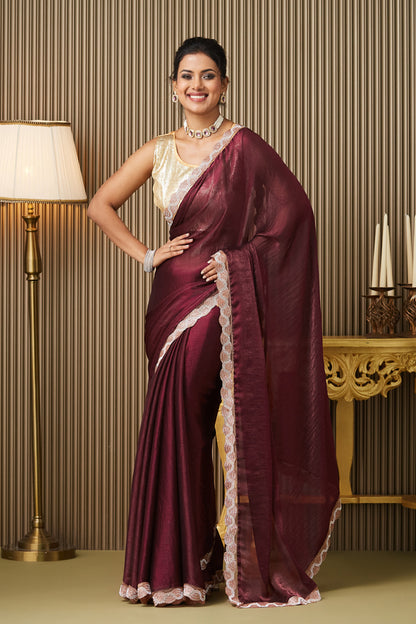 Woman in a maroon saree with white border standing in a room with a lamp and table.