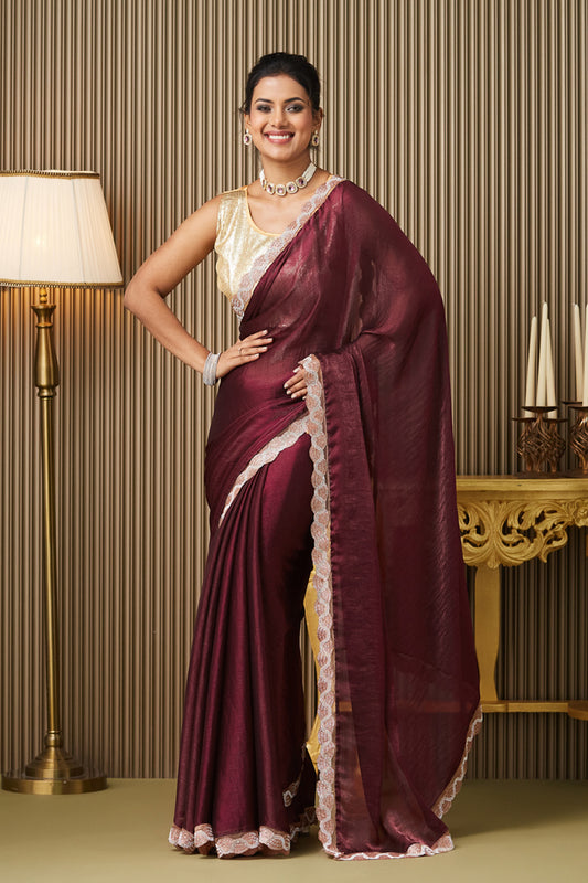 Woman in a maroon saree with white border standing in a room with a lamp and table.